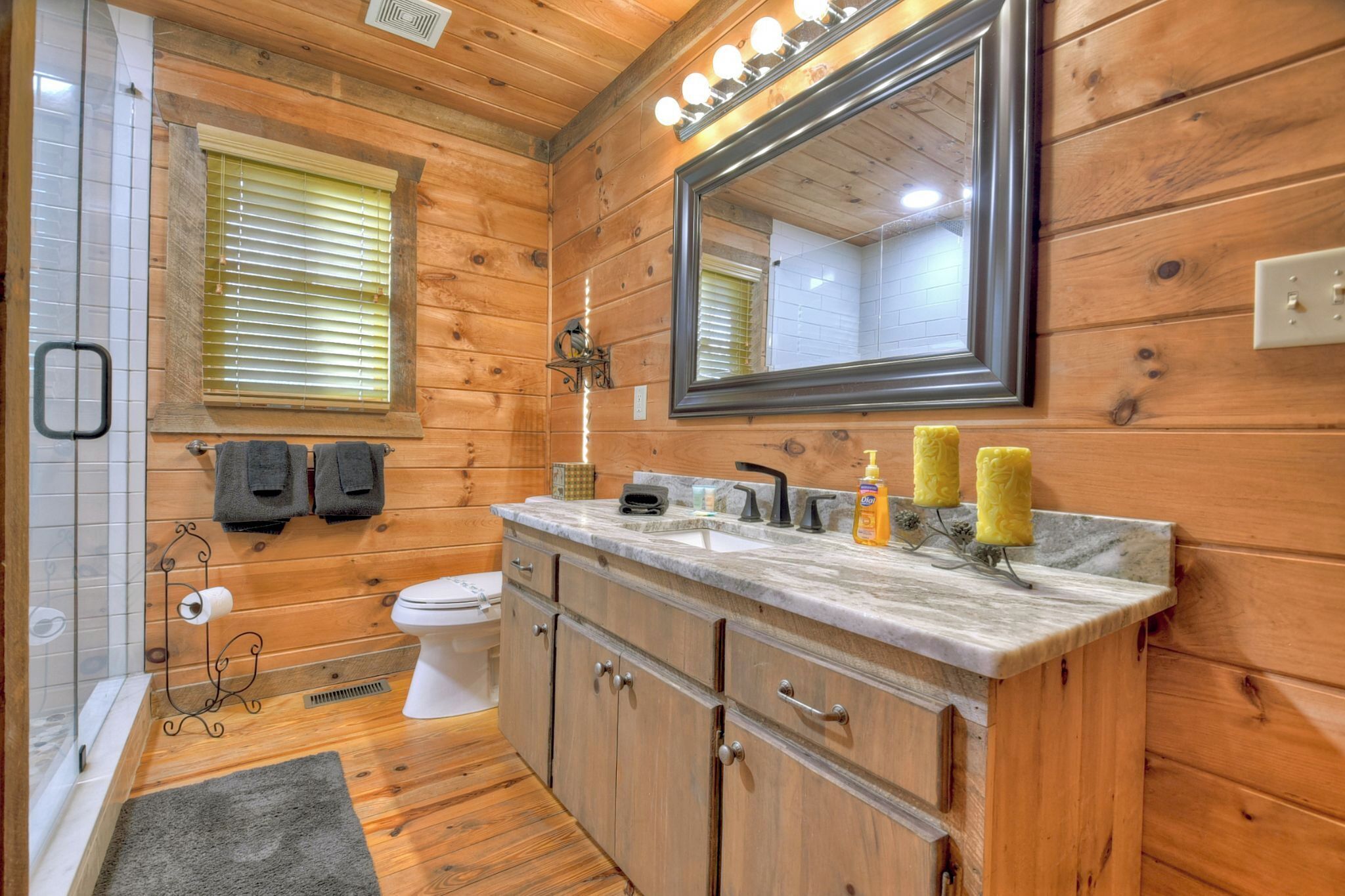 A wooden-paneled bathroom with a toilet, sink, vanity, and mirror.