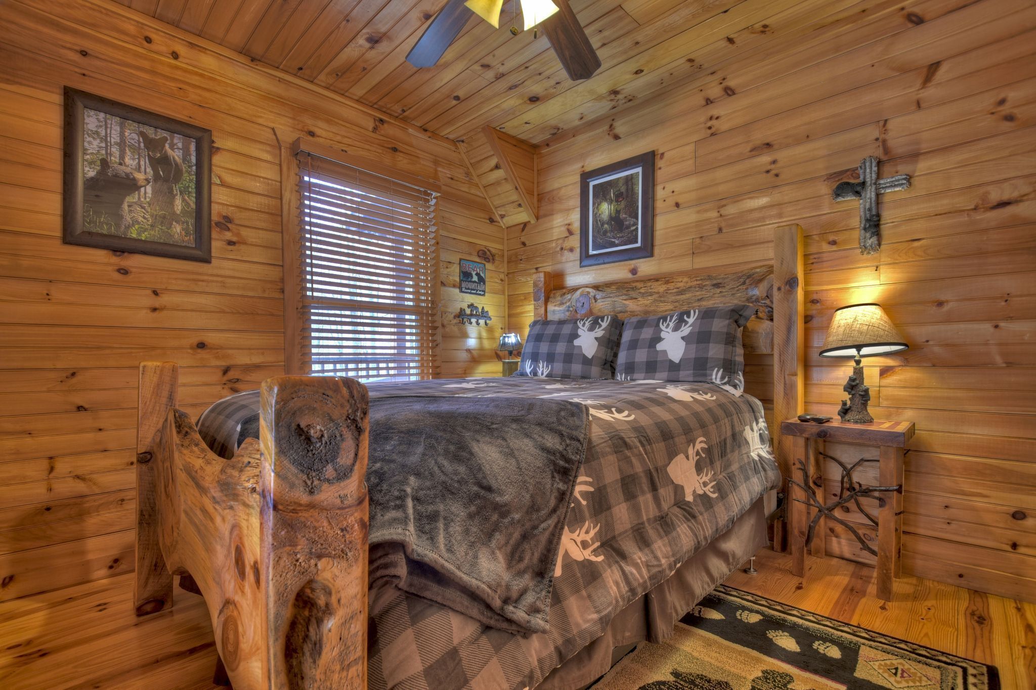 Une chambre confortable aménagée dans un chalet en bois, avec un lit, une tête de lit en bois, une table de chevet avec une lampe et une fenêtre équipée de stores.