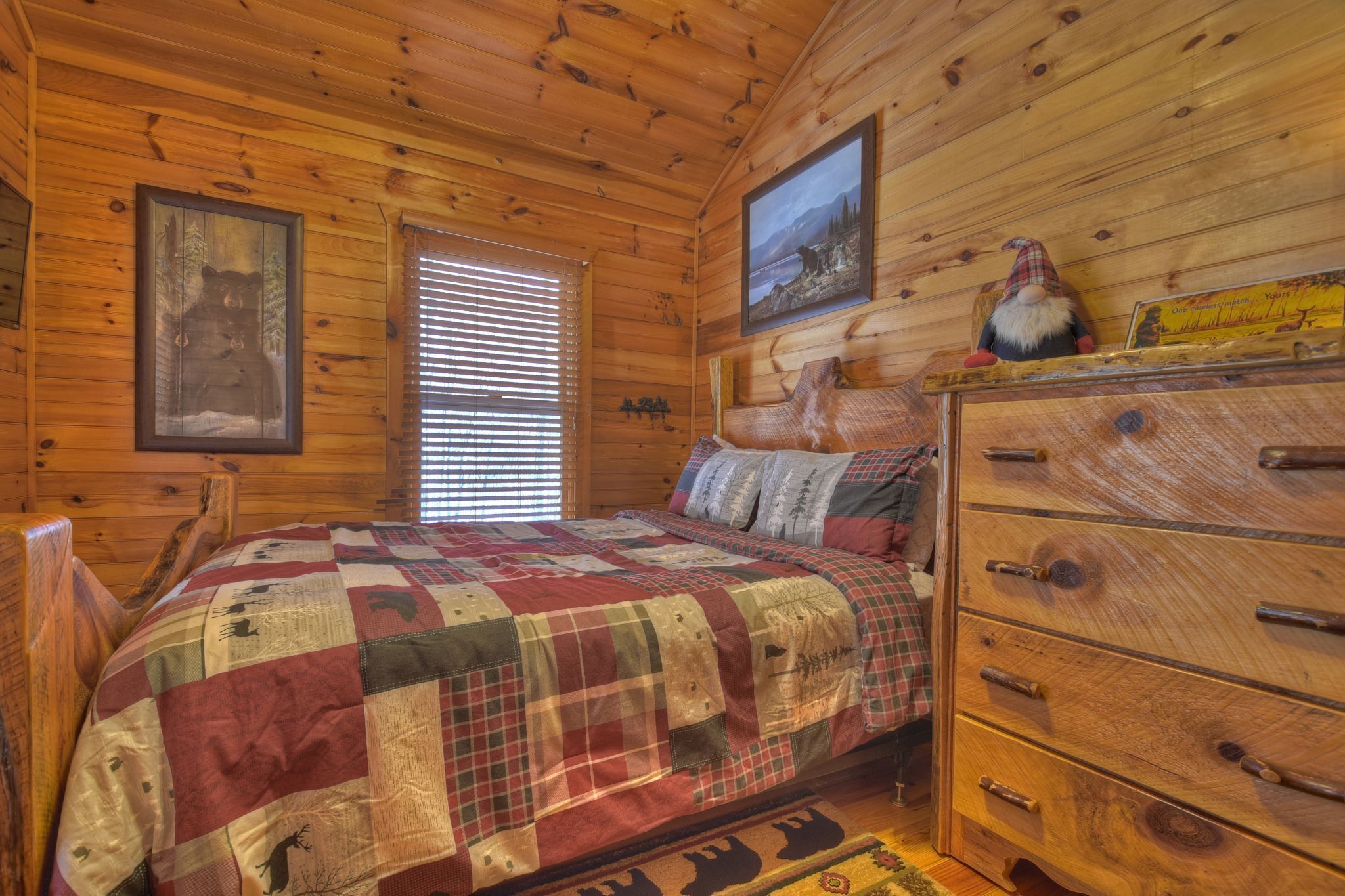 Ein Schlafzimmer einer Holzhütte mit gesteppter Bettdecke, einem Holzschrank und zwei gerahmten Bildern an den Wänden.