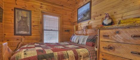 Ein Schlafzimmer einer Holzhütte mit gesteppter Bettdecke, einem Holzschrank und zwei gerahmten Bildern an den Wänden.