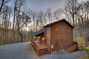 Une cabane en bois avec un porche, une petite terrasse et une allée gravillonnée.