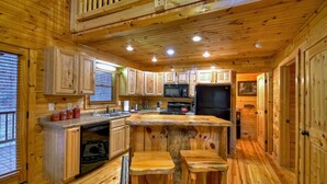 A wooden cabin interior with a kitchen area featuring wooden cabinets, a central island with stools, a built-in microwave, and a refrigerator. - Scenic Views, Hot Tub Soaks, Firepit Roasts, Cookouts & Nearby Adventures - Cardinal's Crossing (Morganton)