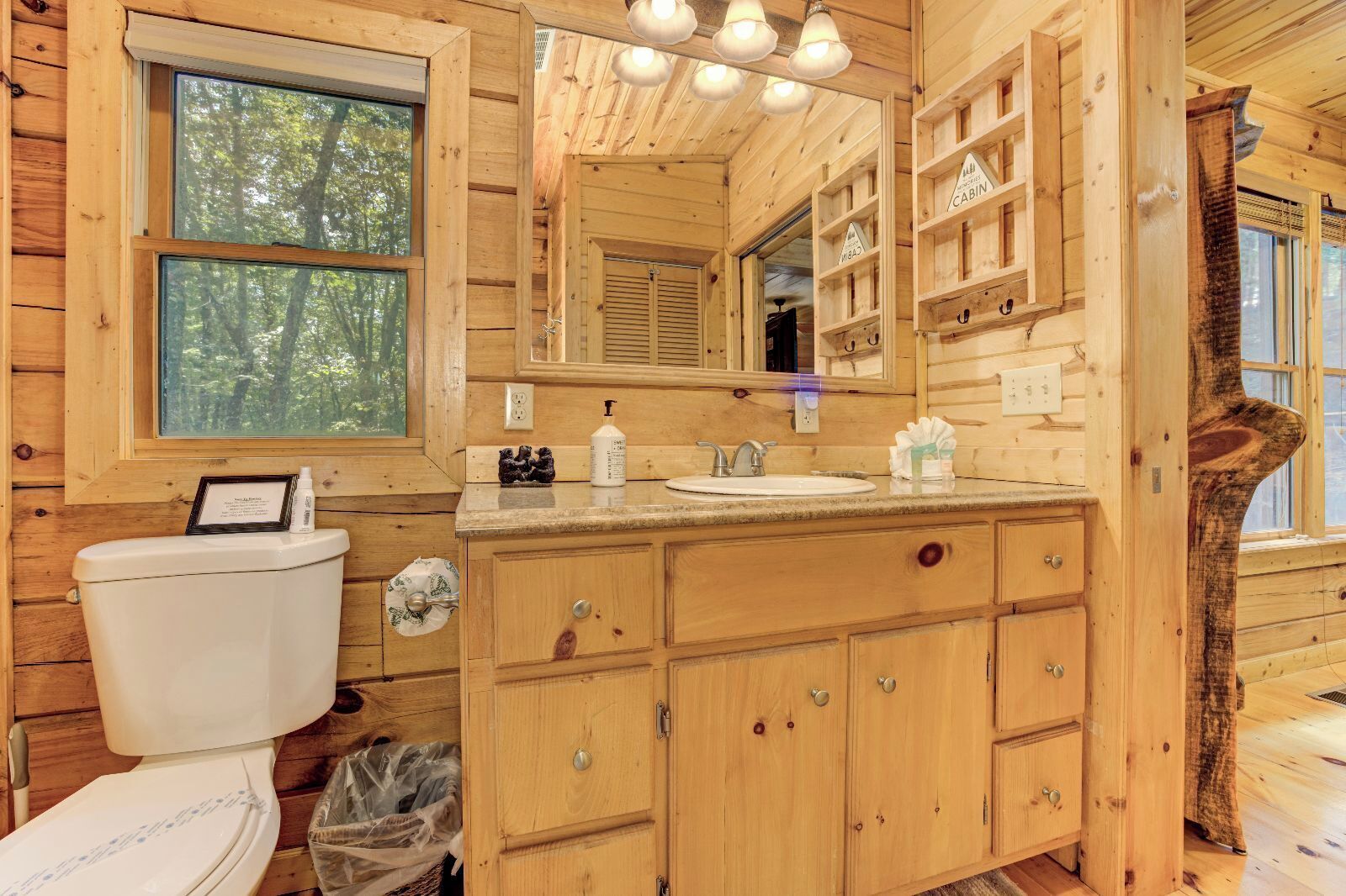 A wooden cabin bathroom with a toilet, sink, cabinets, and a mirror.