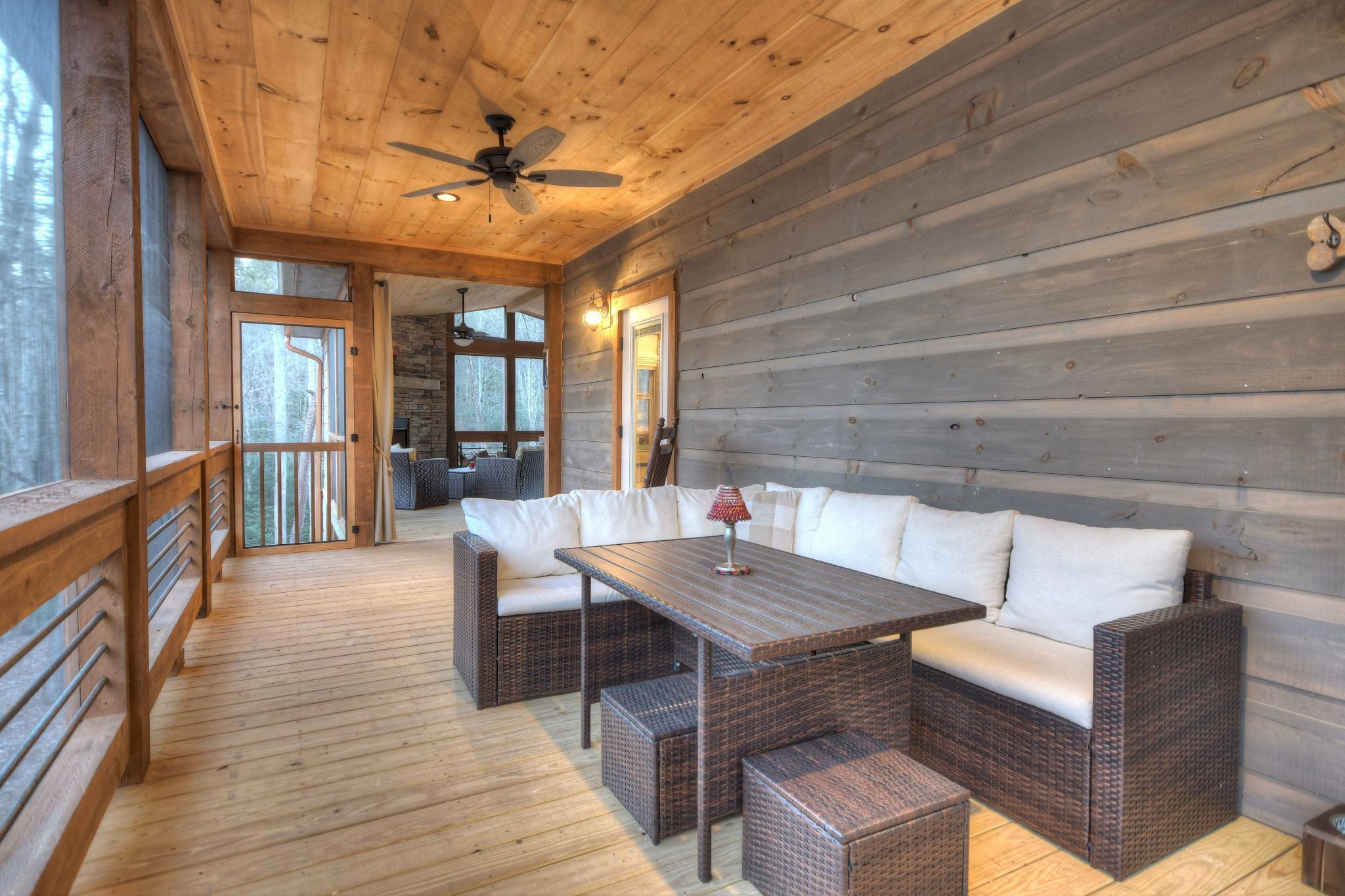 Une terrasse en bois avec des meubles en osier, un ventilateur de plafond et un mur en pierre.