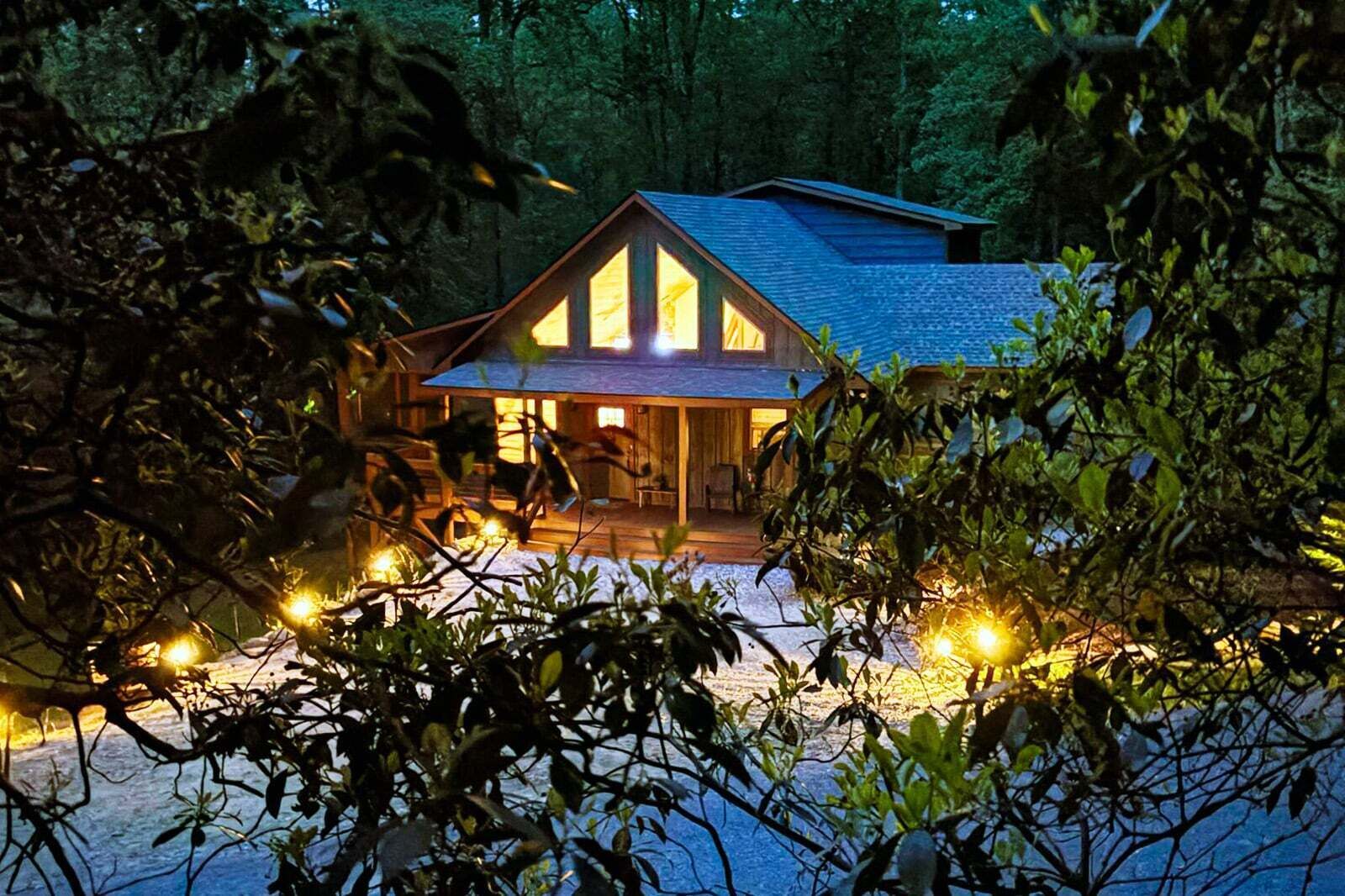 A wooden cabin with a porch, surrounded by trees and lit by string lights.