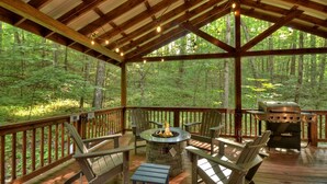 Een overdekt terras met een vuurkorf van steen, Adirondack-stoelen en een barbecue.