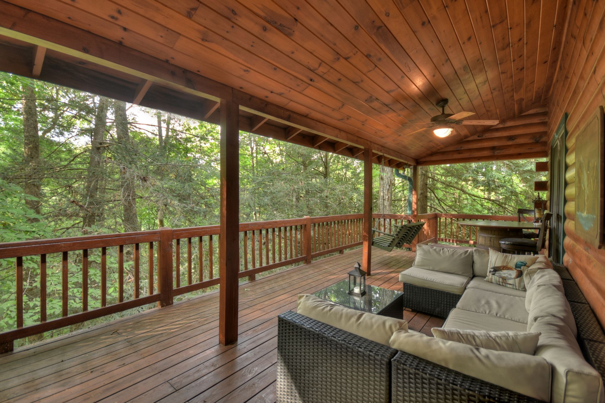 A wooden deck with a sofa and table, overlooking a forested area.