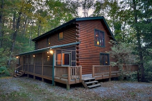 A log cabin with a porch, a deck, and a staircase leading to the entrance.