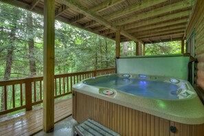 Un bain à remous sur une terrasse en bois, avec vue sur une forêt.