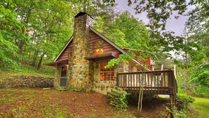 A stone cabin with a wooden deck, surrounded by lush greenery. - Knotty Creek Retreat - Creek access & hot tub (Morganton)