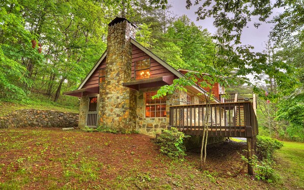 A stone cabin with a wooden deck, surrounded by lush greenery.