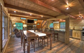 A rustic wooden interior with a dining area, stone fireplace, and a kitchen with wooden cabinets.