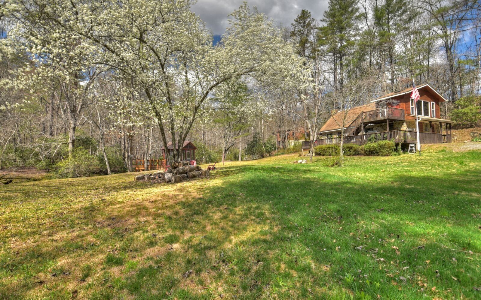 A cabin with a porch, surrounded by trees and a grassy yard.