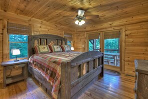 A wooden cabin bedroom with a bed, a nightstand, a ceiling fan, and windows with a view of the outdoors. - Eagles Landing - Gas fireplace, log-cabin feel, close to Blue Ridge, hot tub (Blue Ridge)
