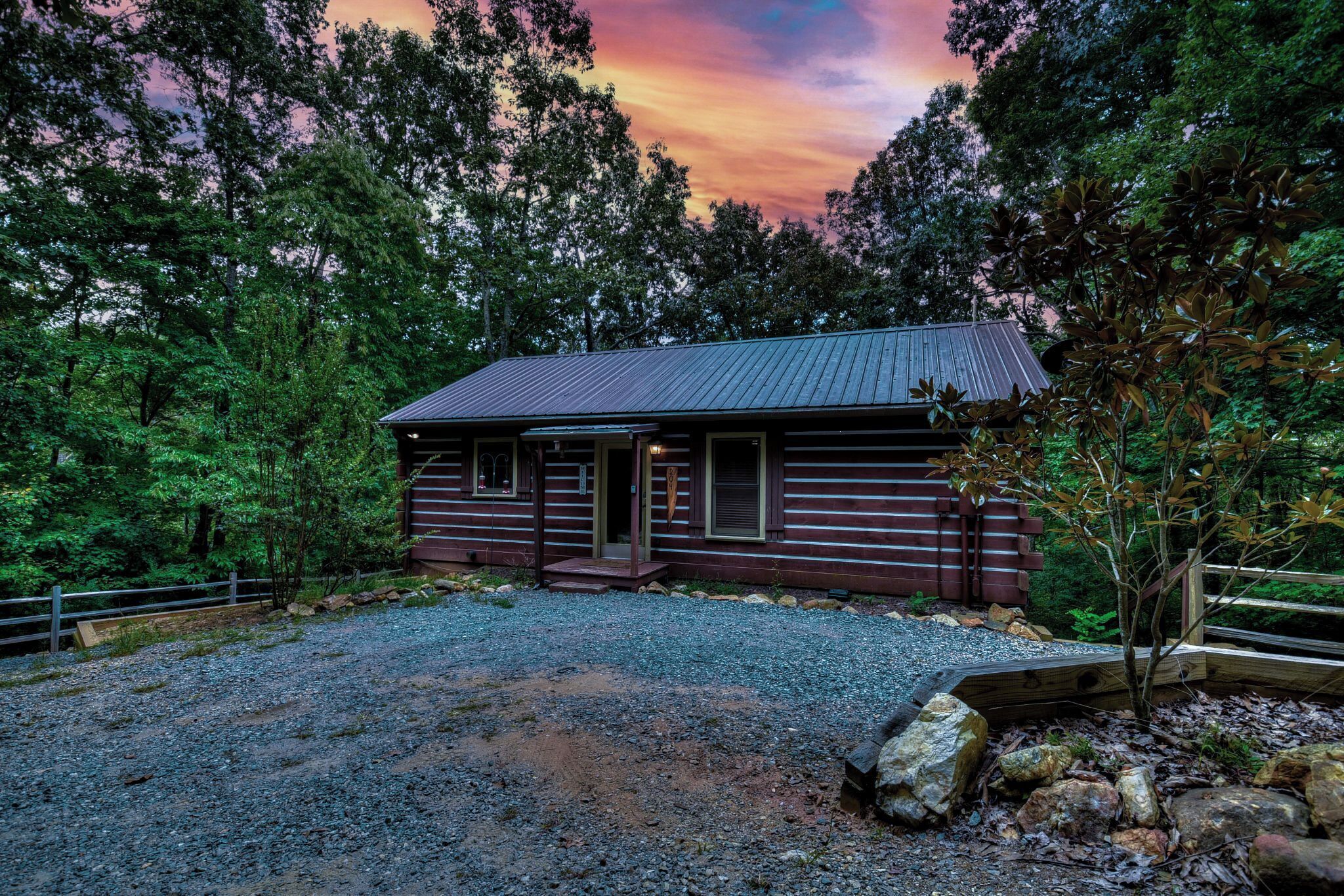 A rustic cabin with a metal roof, surrounded by dense forest.