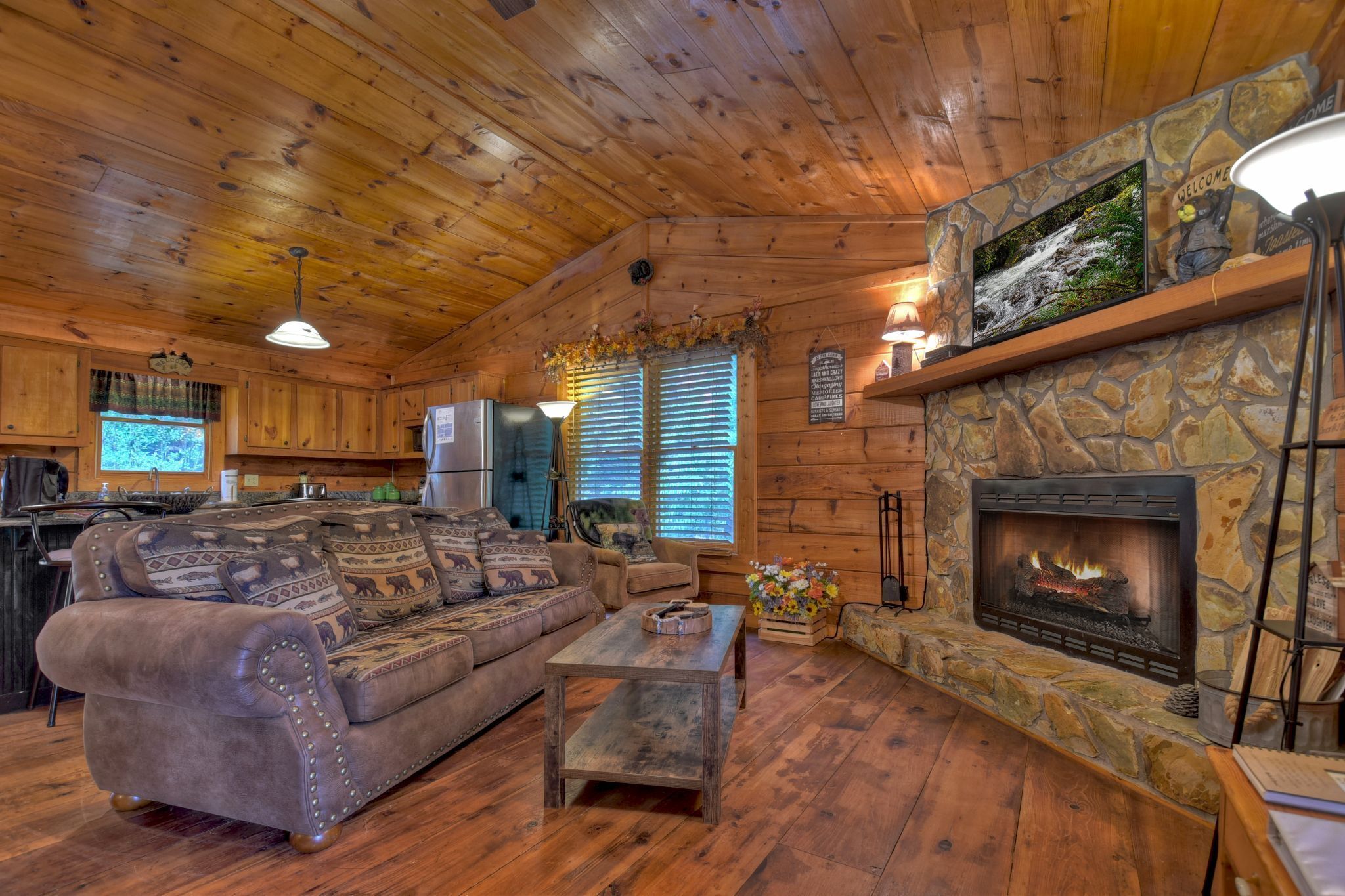 Ein gemütliches Blockhaus mit Kamin aus Stein, Holzbalkendecke und einer Couch mit gemusterten Kissen.
