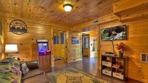 A cozy wooden cabin interior with a leather couch, a television, and a fireplace. - Mama Bear's Hideaway - Hot tub, firepit, and more! (Morganton)