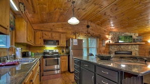 A wooden cabin kitchen with granite countertops, stainless steel appliances, and a stone fireplace. - Mama Bear's Hideaway - Hot tub, firepit, and more! (Morganton)