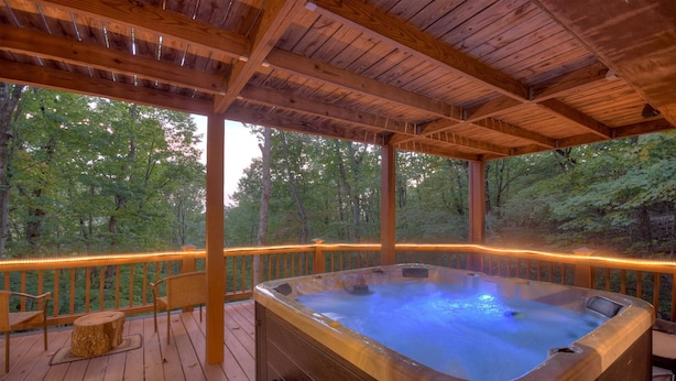 A wooden deck with a hot tub, wooden railings, and a view of the forest. - Mama Bear's Hideaway - Hot tub, firepit, and more! (Morganton)