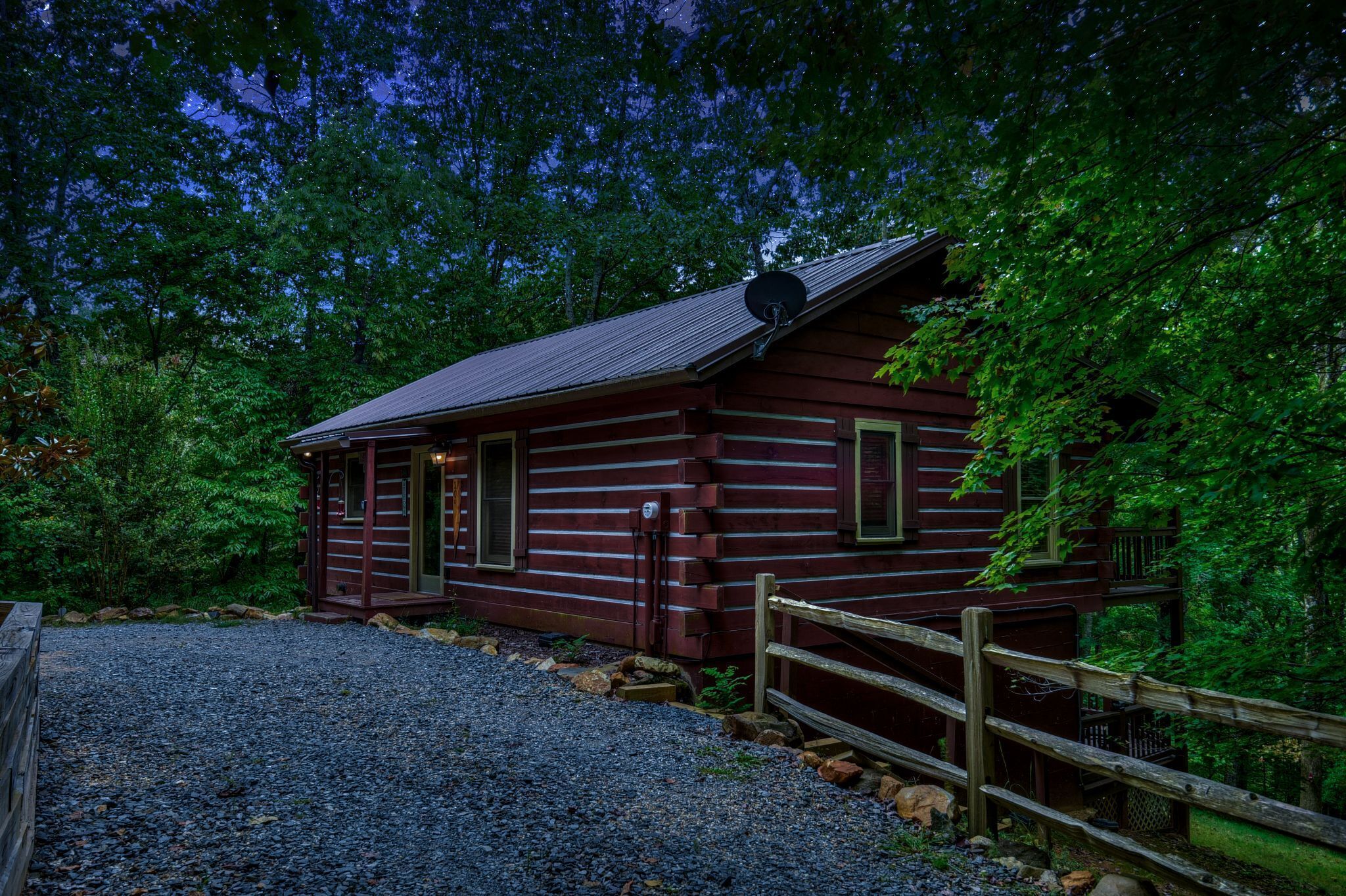 A rustic log cabin with a gravel driveway and a wooden fence.