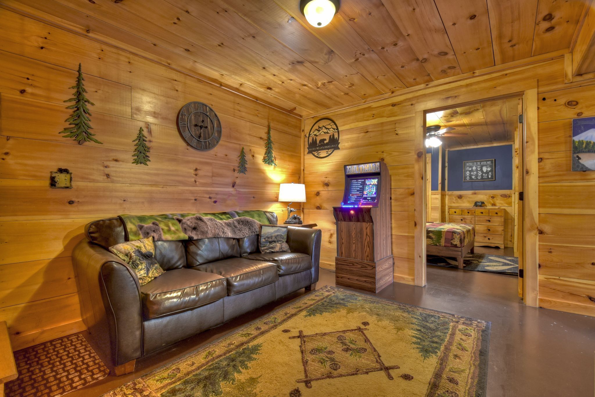 Interior acogedor de una cabaña con un sofá de cuero, paredes de madera, un reloj, una chimenea y una consola de videojuegos.