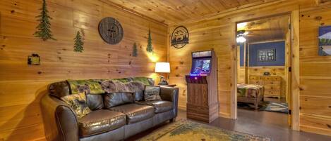 Interior acogedor de una cabaña con un sofá de cuero, paredes de madera, un reloj, una chimenea y una consola de videojuegos.