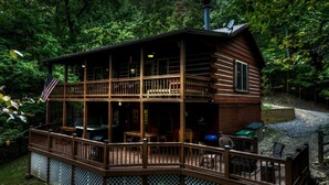 A two-story log cabin with a deck, surrounded by dense forest. - Mama Bear's Hideaway - Hot tub, firepit, and more! (Morganton)