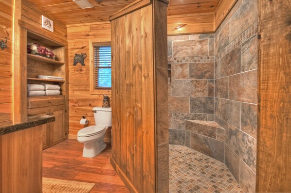 Interior de madera con ducha azulejada, inodoro y estantes con toallas.