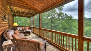 A wooden deck with wicker furniture and a view of a forest.
