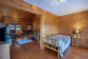 L’intérieur d’un chalet confortable, avec des murs en rondins de bois, un lit en bois, un canapé, un fauteuil et une petite table.