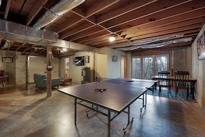 A spacious room with a ping pong table, wooden ceiling beams, and a view through a glass door.