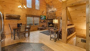 Un intérieur de chalet chaleureux avec une cheminée, des murs en bois, un coin repas et un mur décoratif en pierre.