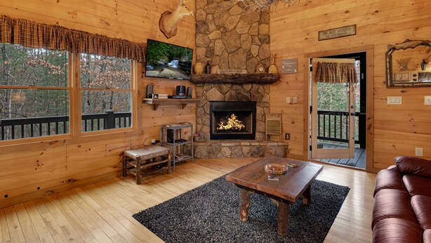 L’intérieur chaleureux d’un chalet avec une cheminée en pierre, des murs en bois, un téléviseur et un banc.