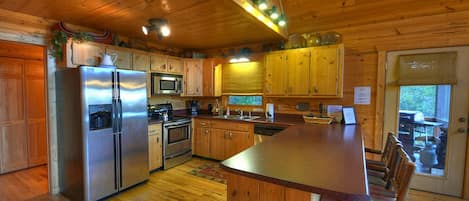 Une cuisine rustique, située dans une cabane en bois, avec un îlot central, des appareils en acier inoxydable et des armoires en bois.