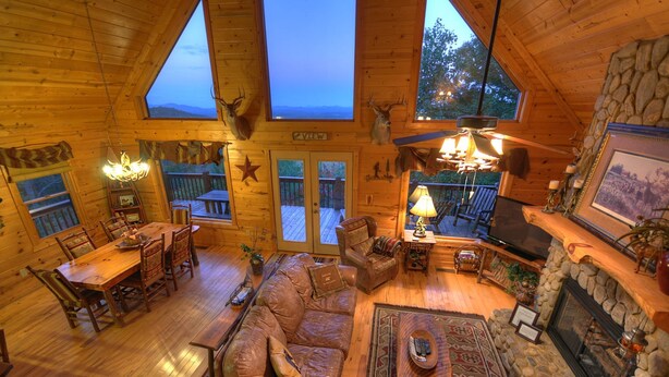 Interior acogedor de una cabaña de madera con zona de comedor, asientos, chimenea y trofeos de animales.