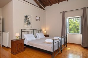 A bedroom with a bed, two bedside lamps, a radiator, a wooden cabinet, and a window with curtains.