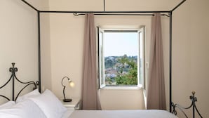 Ein Schlafzimmer mit einem Metallbettgestell, einem Nachttisch mit Lampe, einem Fenster mit Vorhängen und Blick auf eine Stadt.