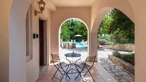 Eine überdachte Terrasse im Freien mit Tisch und Stühlen, einem Pool und einer Steinmauer.