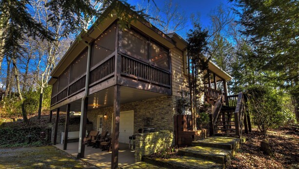 Une cabane à deux étages dotée d’un balcon, de fondations en pierre et d’une terrasse en bois.