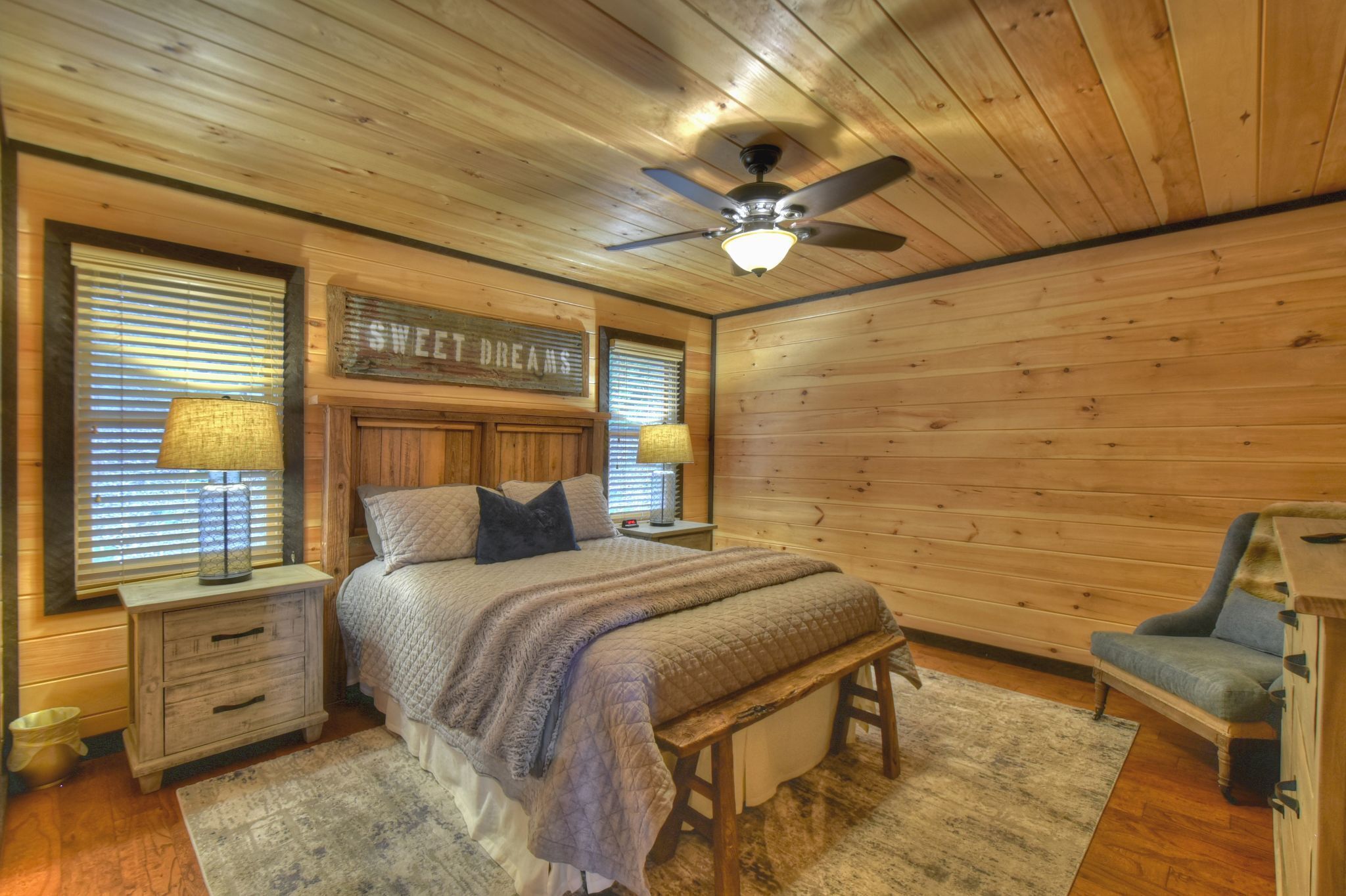 Une chambre confortable, aménagée dans un chalet en bois, avec un lit, des tables de chevet, un banc, une chaise et un ventilateur de plafond.