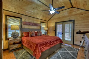 A bedroom with a wooden ceiling, a bed with a red blanket, a nightstand with a lamp, and a telescope. - Skyfall - Stunning mountain views, cozy hot tub, comfy beds, game room, and more! (Mineral Bluff)