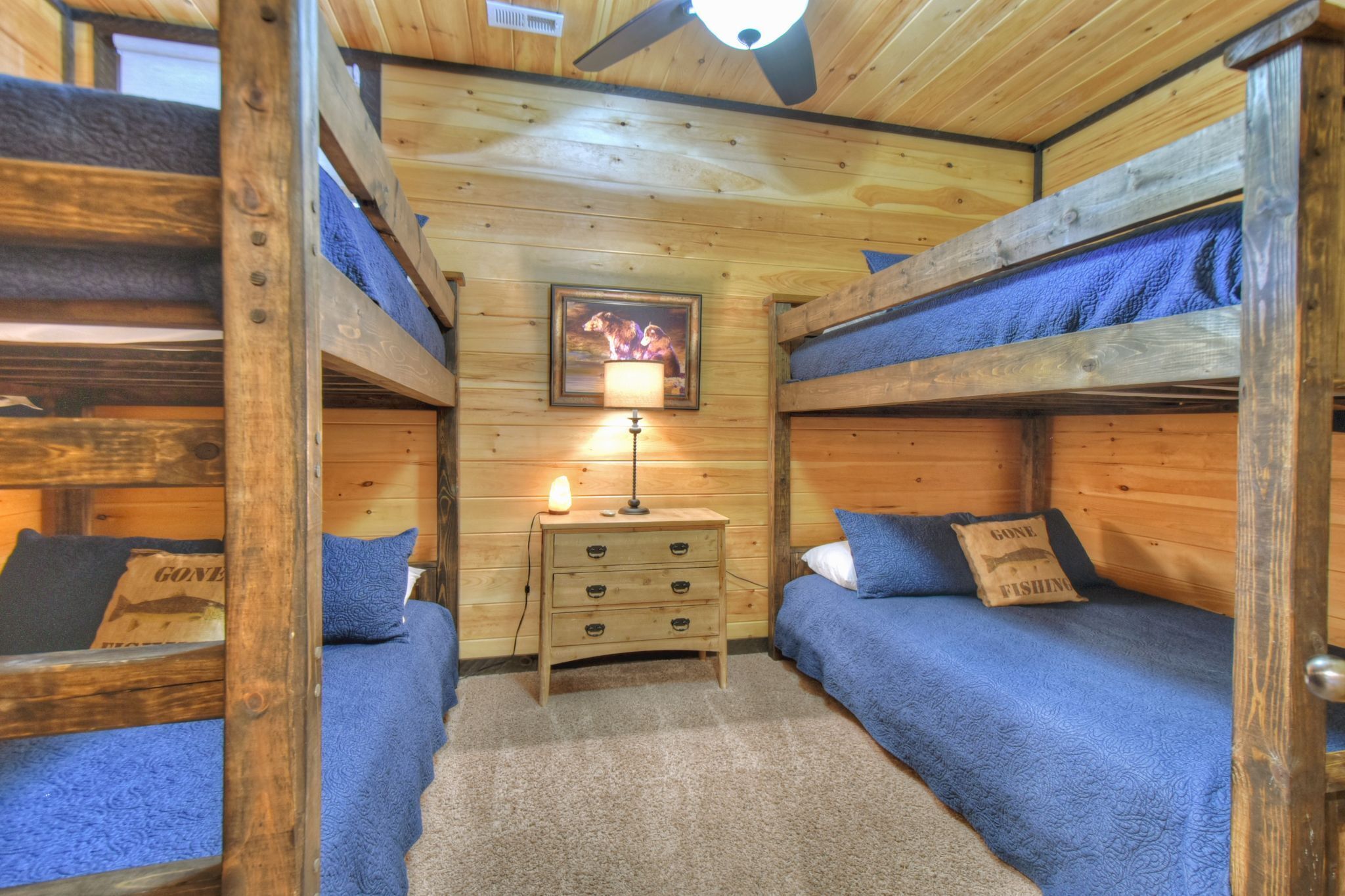 A cabin with bunk beds, a small wooden dresser, and a ceiling fan.