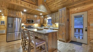 Cocina de cabaña de madera con una isla central, electrodomésticos de acero inoxidable y una terraza de madera afuera.