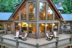 A large wooden cabin with multiple large windows, a deck with chairs, and a visible grill area.