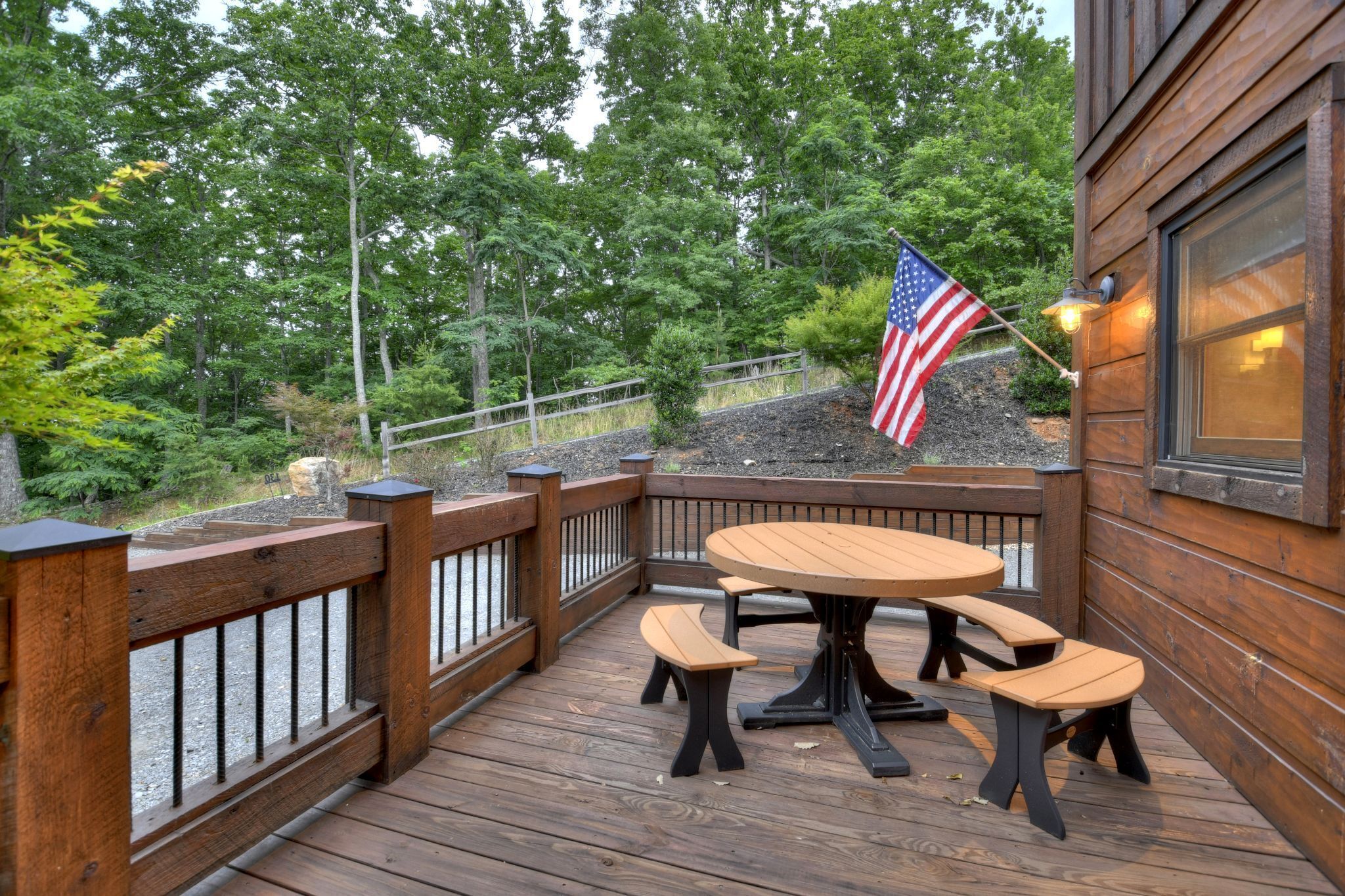 Une terrasse en bois avec une table ronde et des bancs, entourée d’une balustrade en bois, et un drapeau américain.