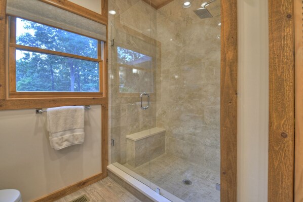 A modern bathroom with a glass-enclosed shower, a wooden window, and a white towel hanging on a rack.