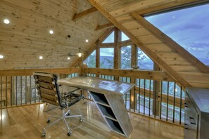 A spacious loft with a high ceiling, a large desk, and a view of the outdoors.