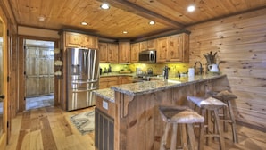 A wooden cabin-style kitchen with a central island, stainless steel appliances, and bar stools. - Relax in private rustic luxury! - A Starry Night (Cherry Log)