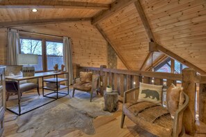 A cozy cabin interior with wooden walls, a dining table, chairs, and a rustic sofa.