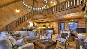 A spacious loft-style room with a high ceiling, wooden beams, a cozy seating area with a sofa and armchairs, a dining table, and a kitchen in the background. - Relax in private rustic luxury! - A Starry Night (Cherry Log)